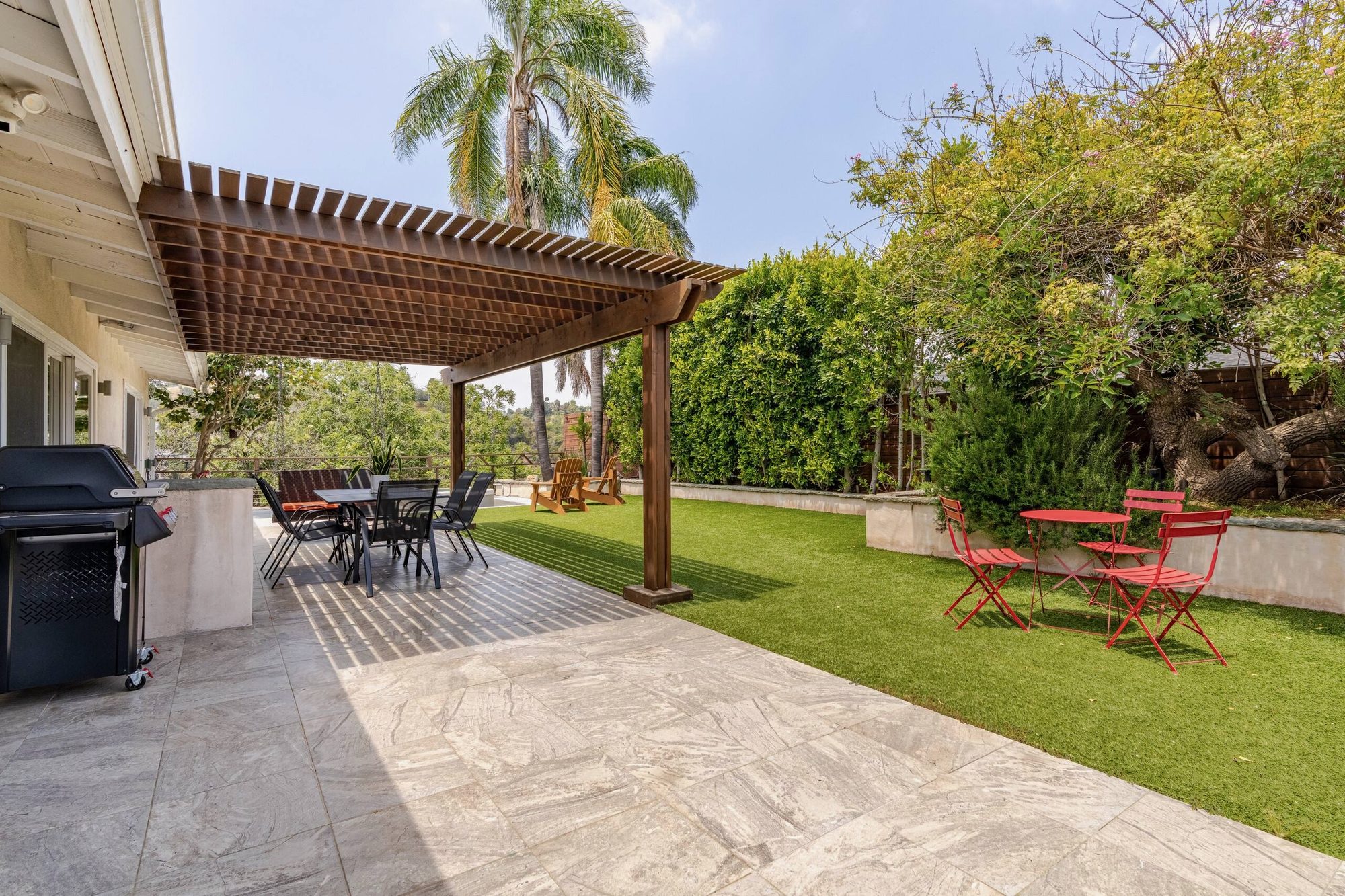 Patio dining table and hanging bench under pergola with hillside behind