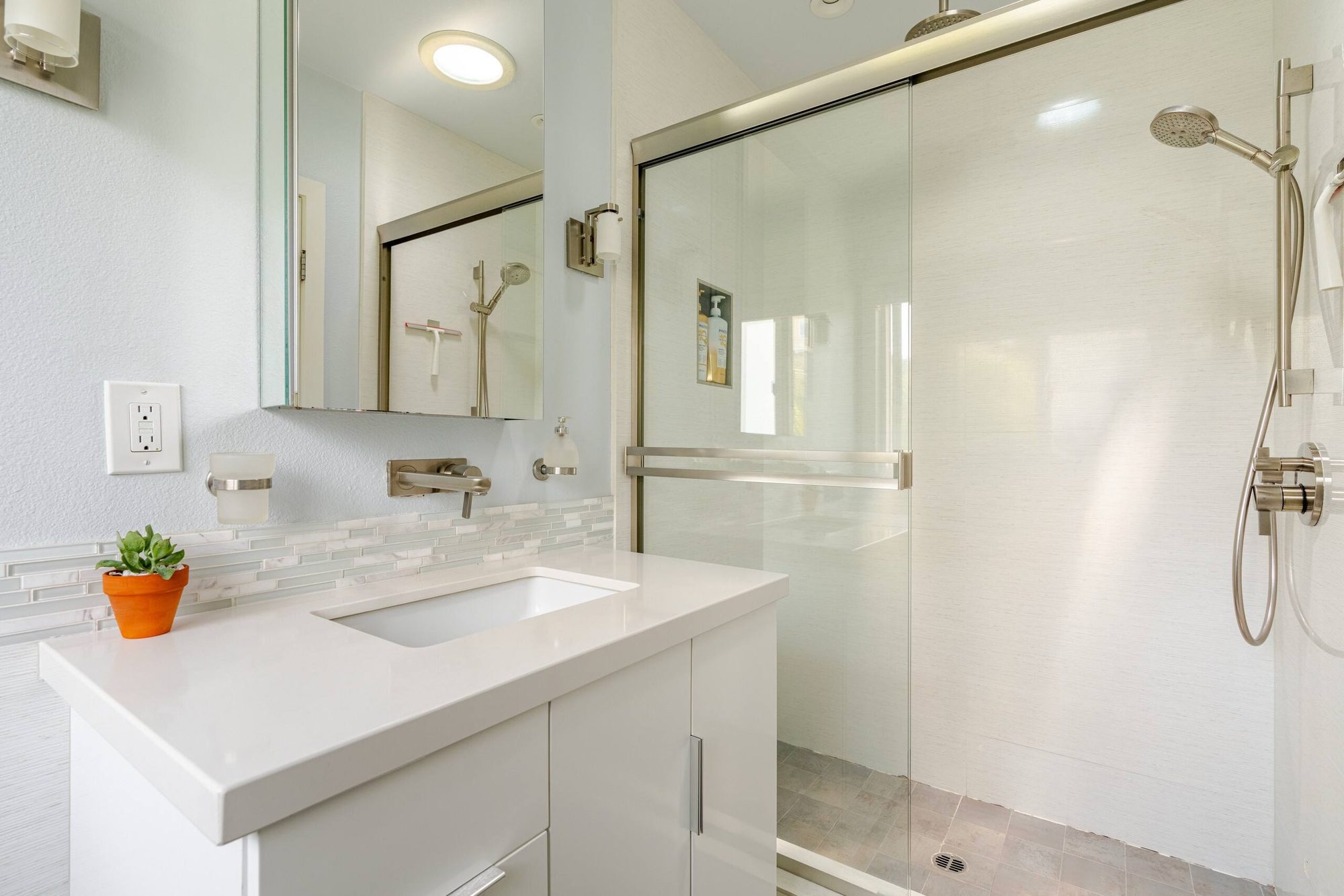 Bathroom vanity beside the glass shower enclosure with rainfall showerhead