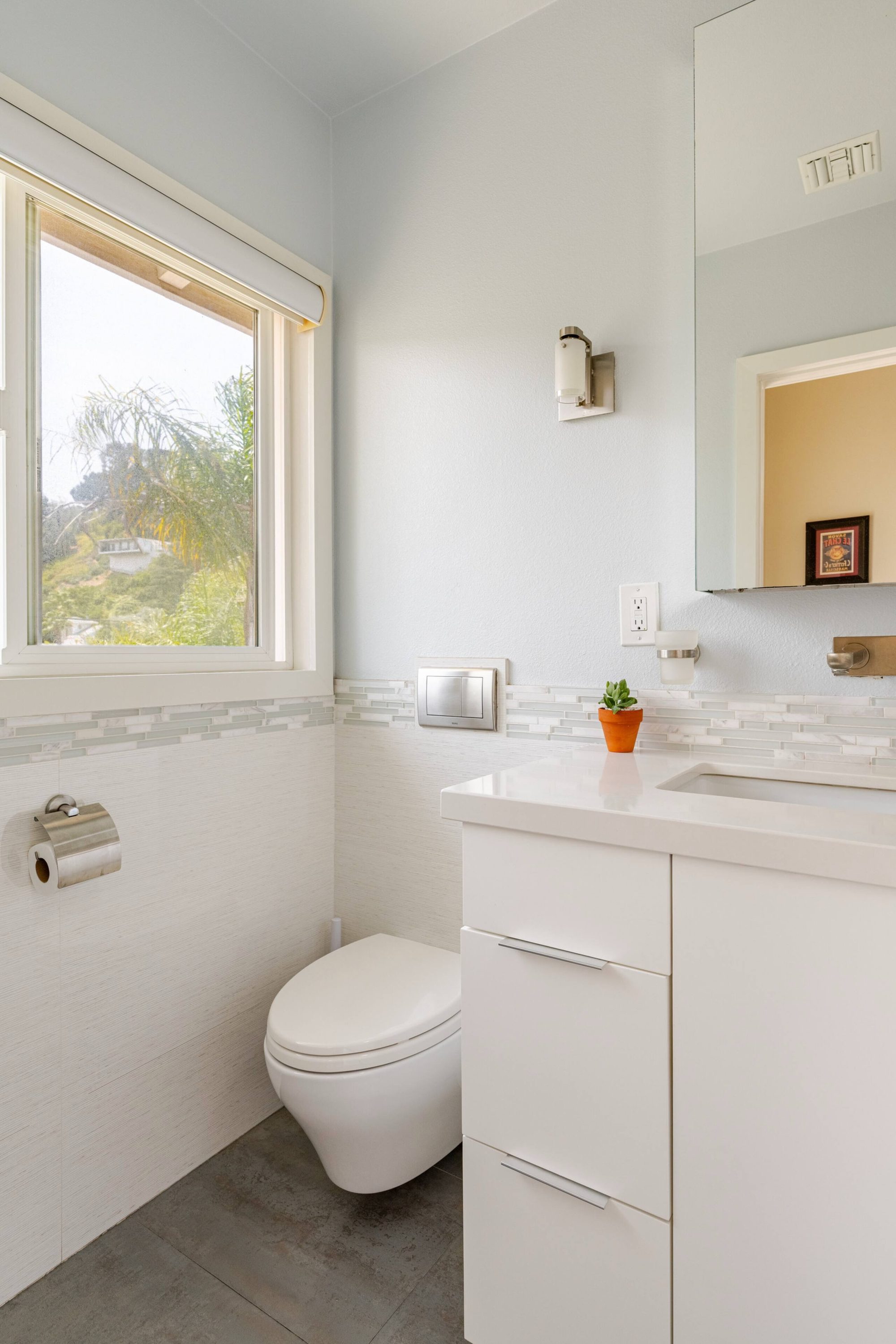 Bathroom toilet beneath a window with a hillside view, beside the vanity and mirror