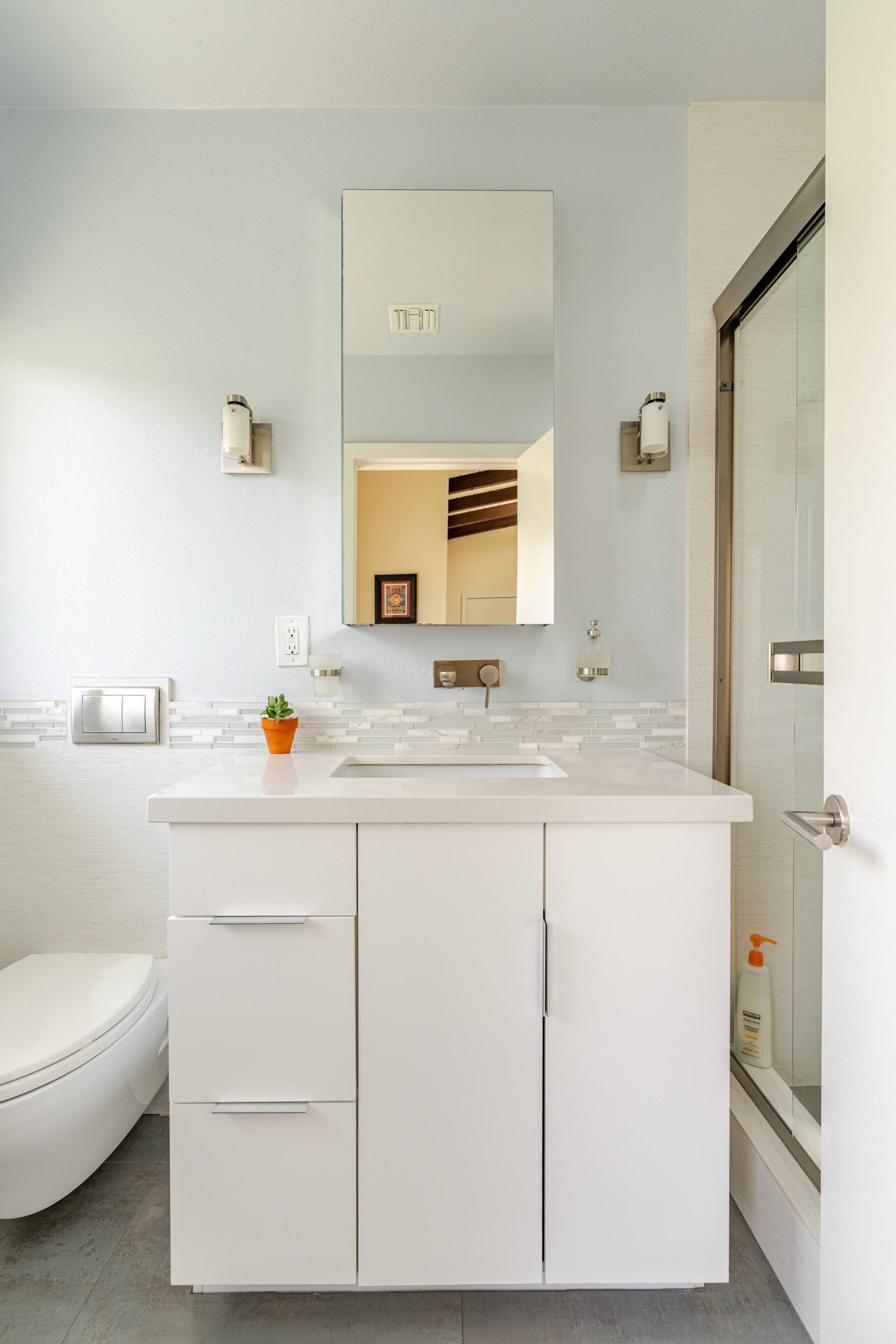 Bathroom vanity with mirrored medicine cabinet, mosaic tile backsplash, and glass shower door