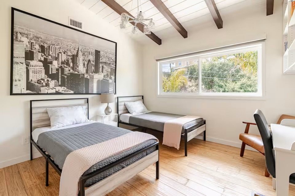 Bedroom with two beds, a large black-and-white city skyline photograph, and a hillside view through the window