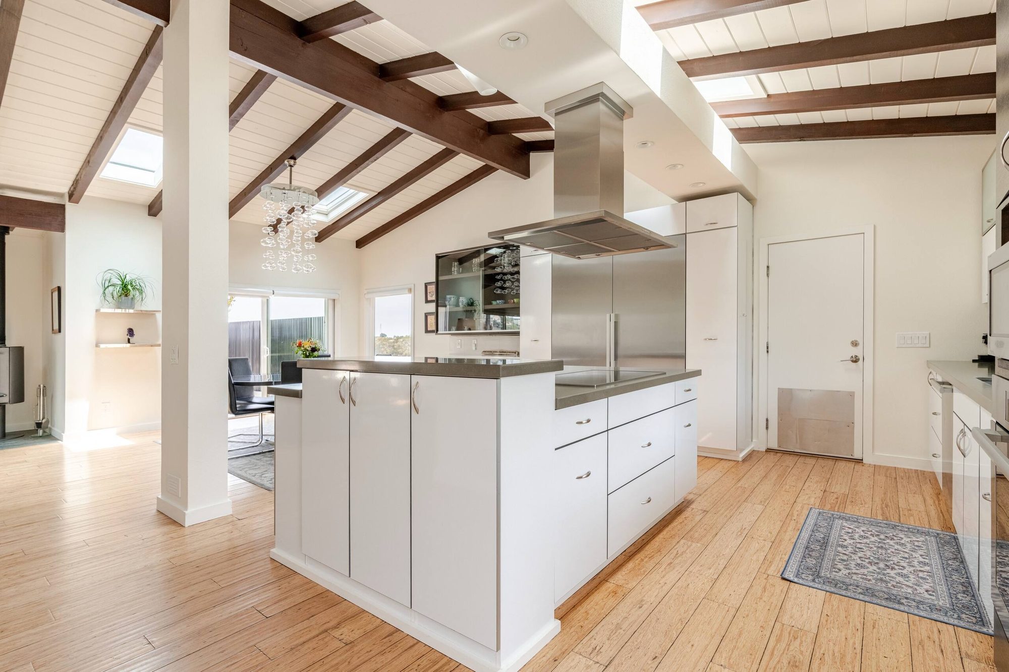 Wide kitchen view with island, stainless range hood and skylights, looking toward the dining room