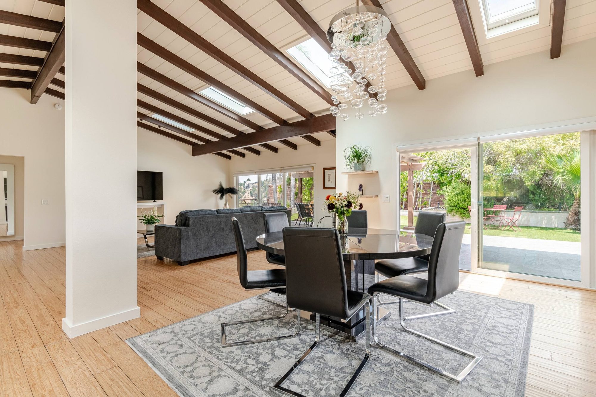 Open living and dining room with vaulted beamed ceiling, skylights, and glass chandelier