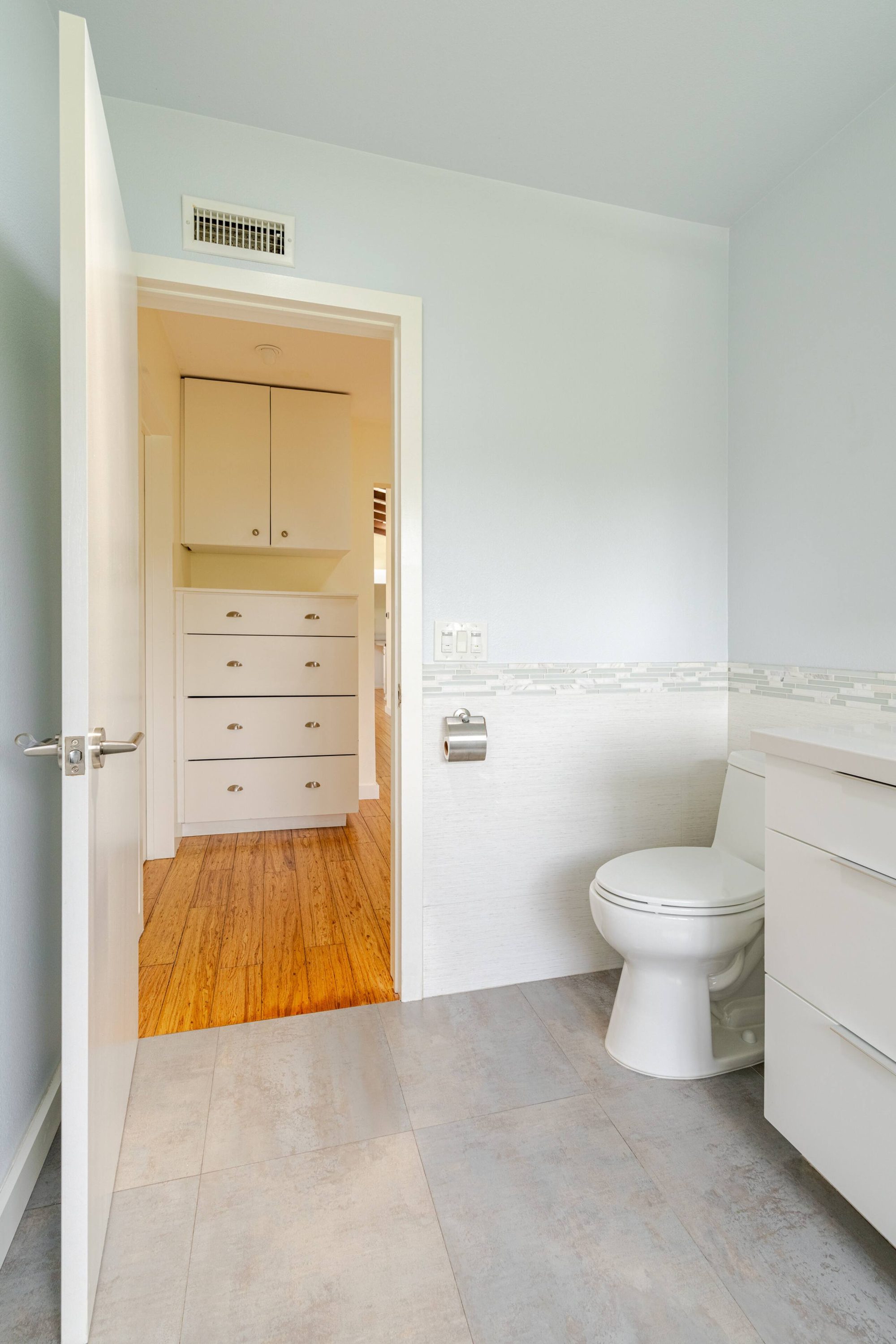Primary bathroom toilet with a doorway view into an adjoining dressing room with built-in drawers