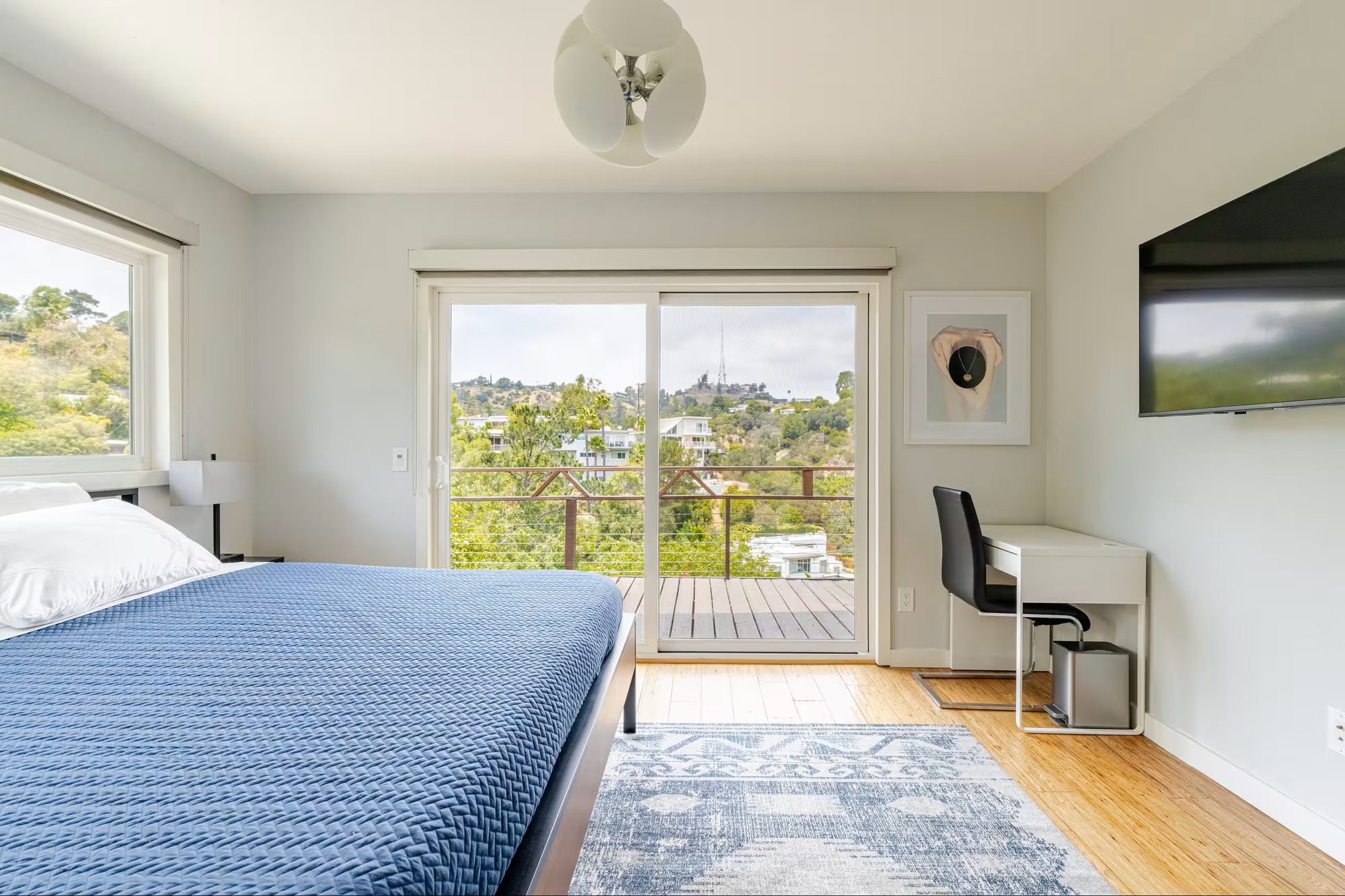 Bedroom desk beside a sliding glass door leading to a private deck, with a view toward the Hollywood Sign and Griffith Observatory in the distance